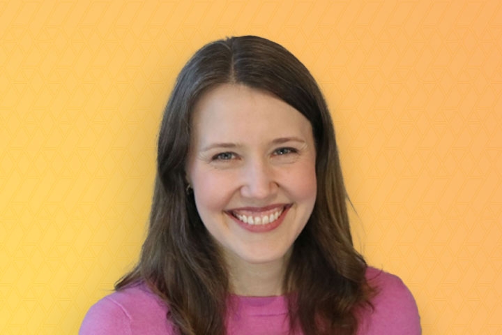 Close up photo of Jaclyn Donahue with long dark hair and a pink shirt on a yellow background